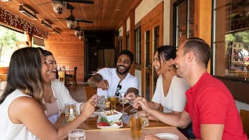 A group of people toasting at a wooden table with drinks and snacks in a restaurant with a wooden interior and large windows.