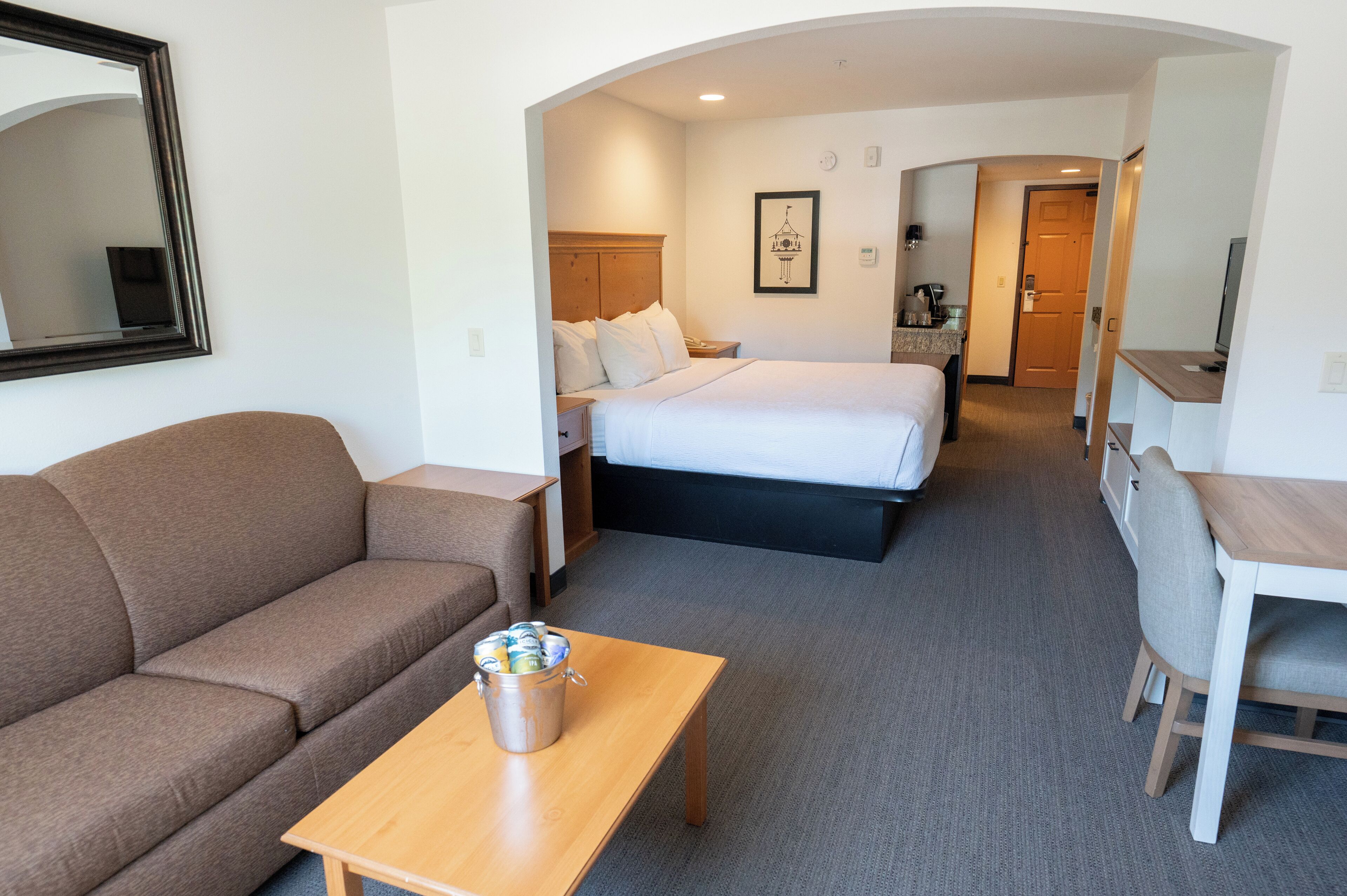 Une chambre d’hôtel avec un canapé, un lit, une table en bois avec un seau, un bureau et une chaise.