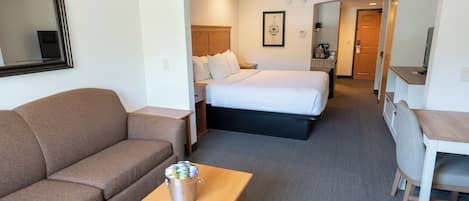 A hotel room with a sofa, a bed, a wooden table with a bucket, a desk, and a chair.