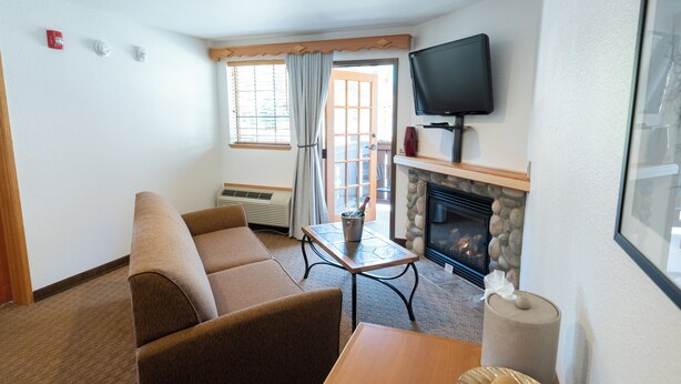 A living room with a sofa, a table, a fireplace, and a television. - Icicle Village Resort (Leavenworth)