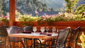 Mesa de madera dispuesta con cuatro sillas, vasos y un plato, con vistas a un paisaje con flores y una barandilla de madera.