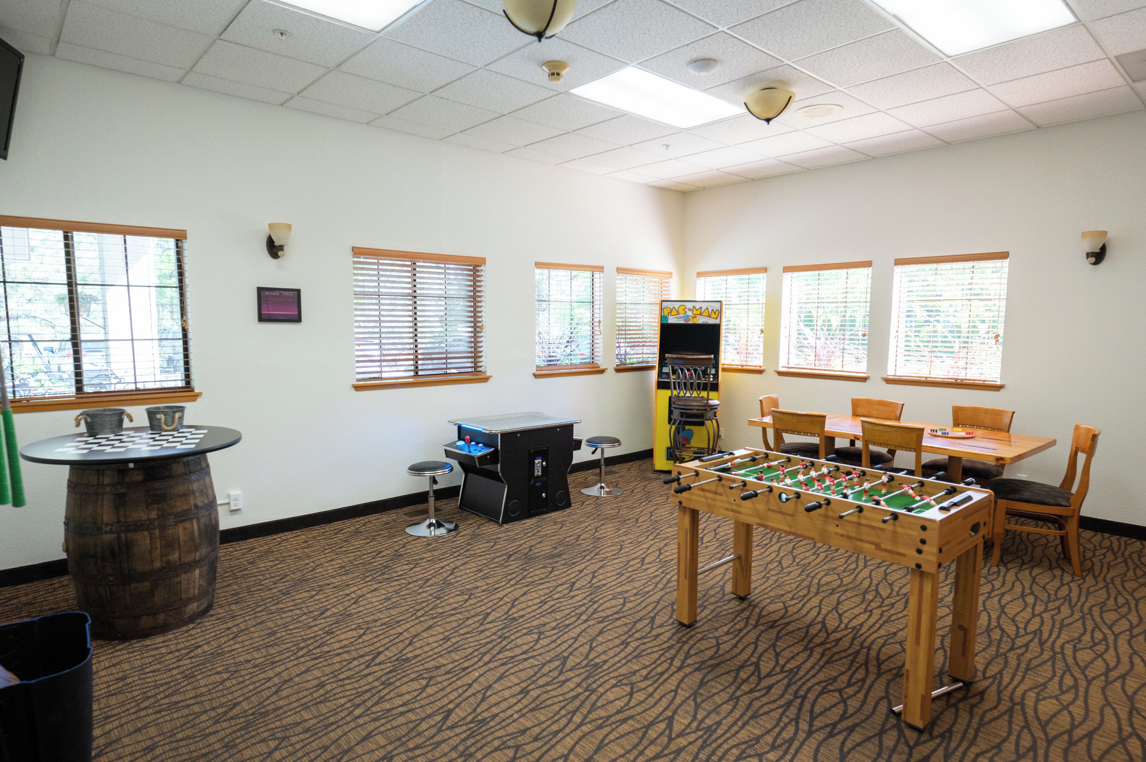A room with a foosball table, a pool table, and a bar area with stools.