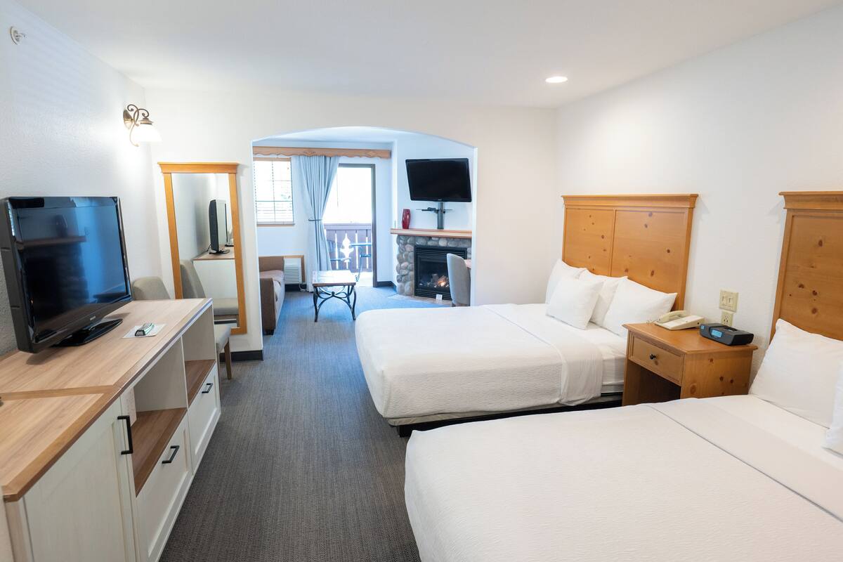 A hotel room with two beds, a TV, a desk, a chair, a fireplace, and a balcony with a view.