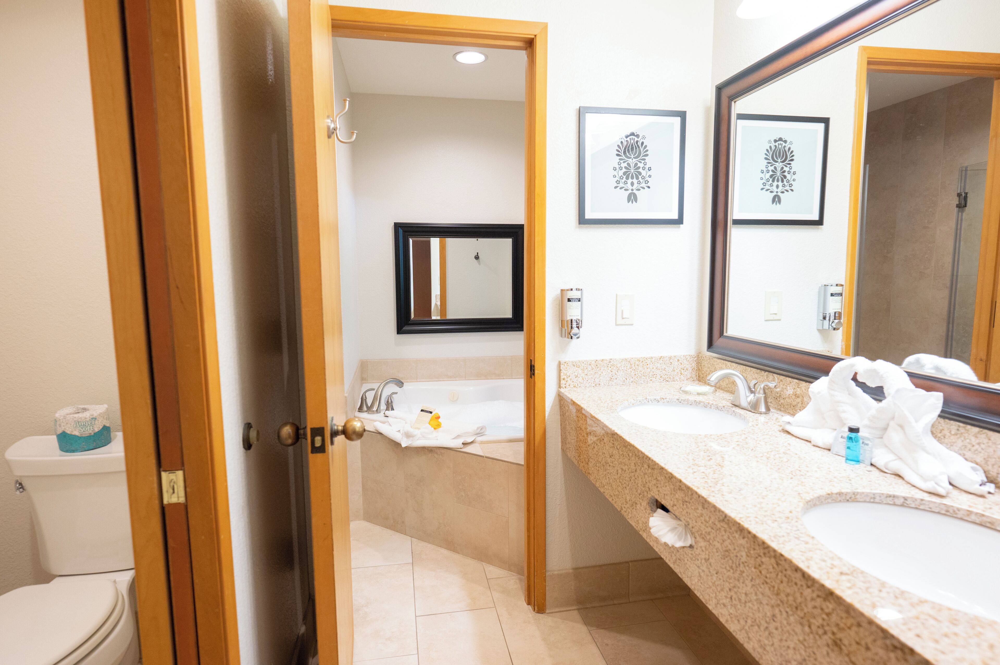 A hotel bathroom with two sinks, a bathtub, and a toilet.