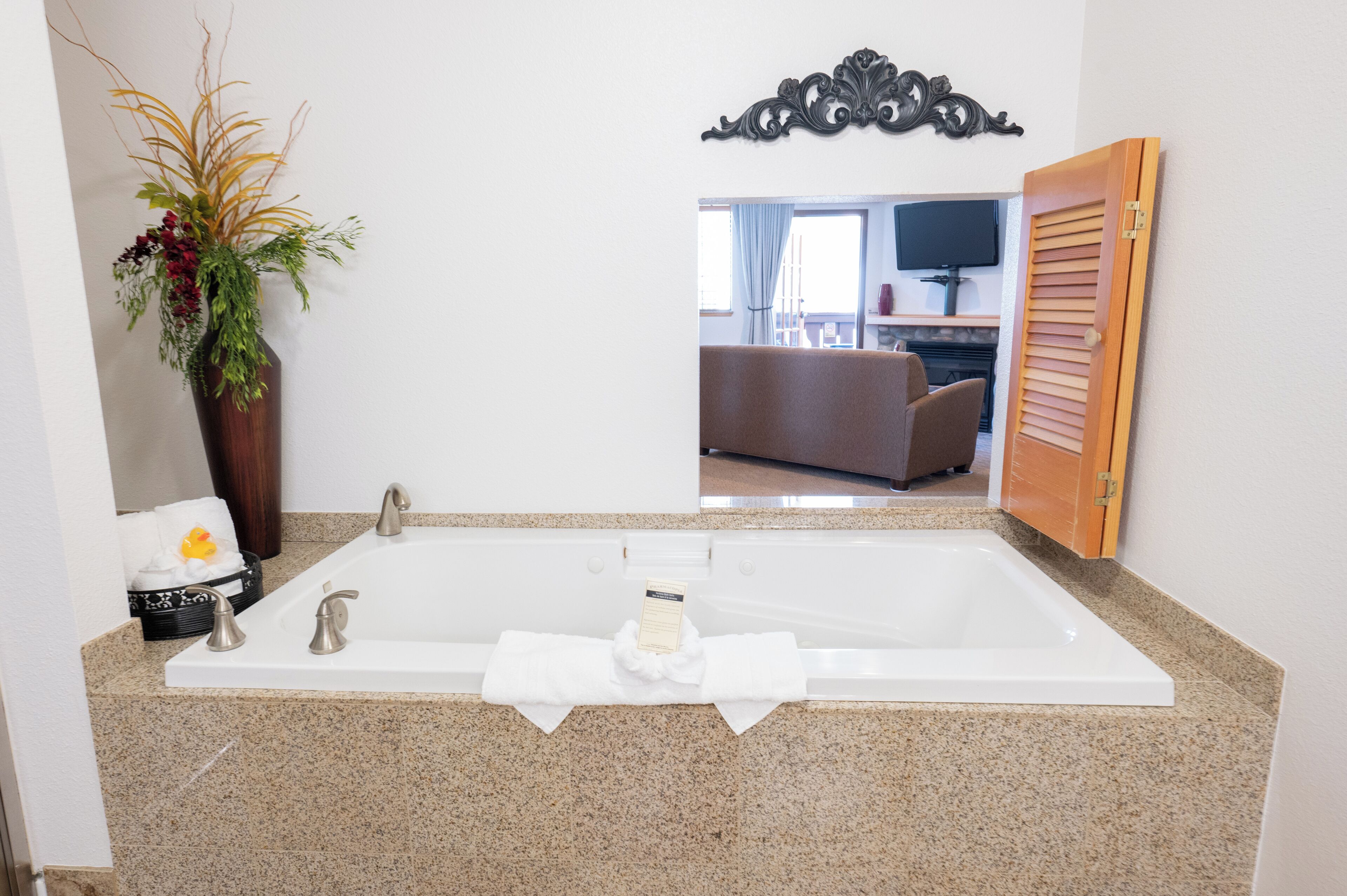 Un baño moderno con una bañera grande, una planta decorativa y un espejo que refleja una sala de estar.