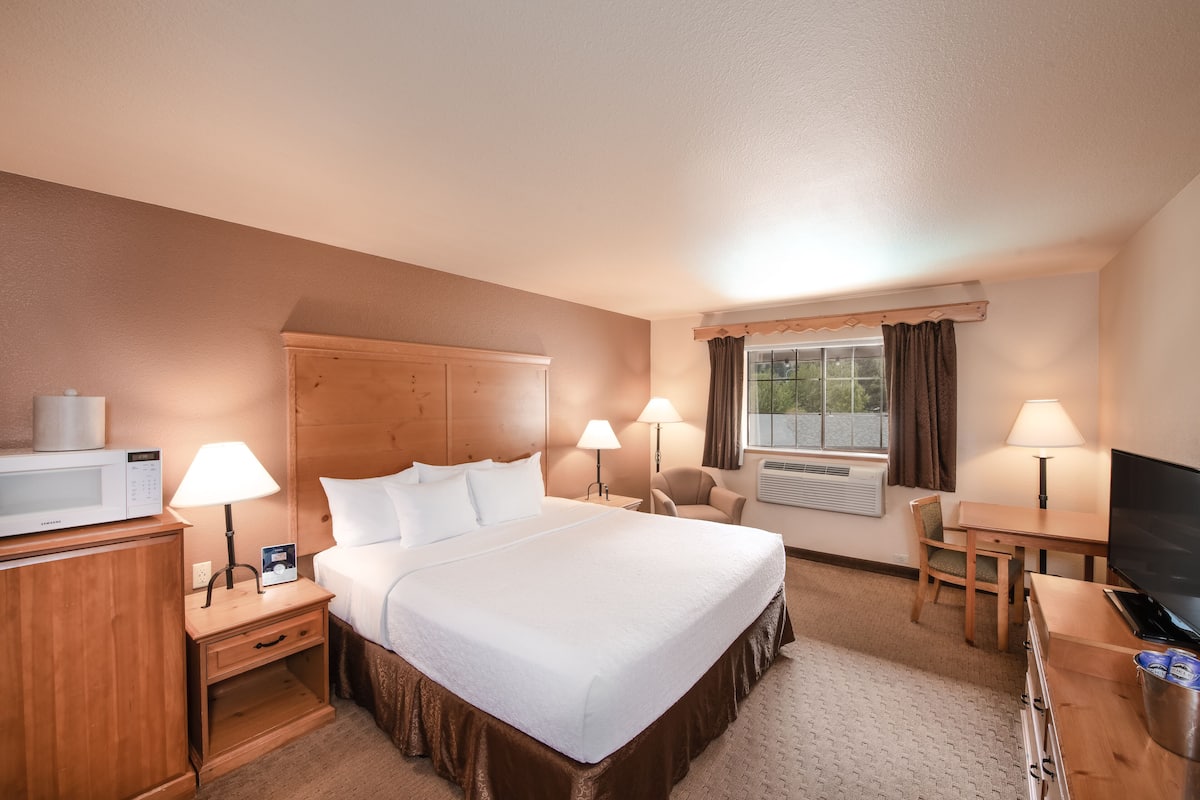A hotel room with a large bed, bedside tables with lamps, a TV, a desk, and a window with curtains.