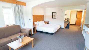 A hotel room with a bed, a sofa, a small table with a bottle, a wooden headboard, and a framed picture on the wall.