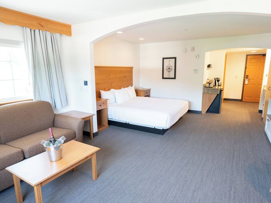 A hotel room with a bed, a sofa, a small table with a bottle, a wooden headboard, and a framed picture on the wall.