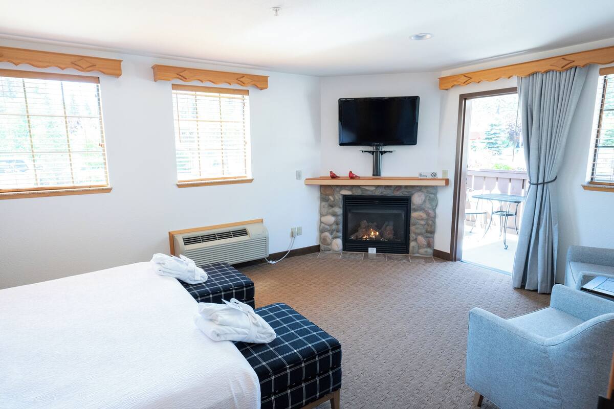 A hotel room with a bed, two ottomans, a flat-screen TV, a fireplace, and a view of the outdoors.
