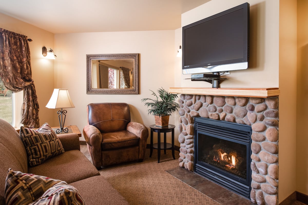 A living room with a fireplace, a leather armchair, a sofa, a television, and a mirror.