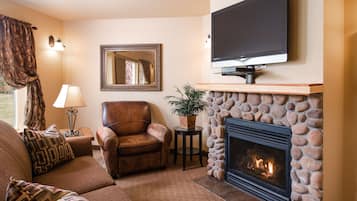 A living room with a fireplace, a leather armchair, a sofa, a television, and a mirror.