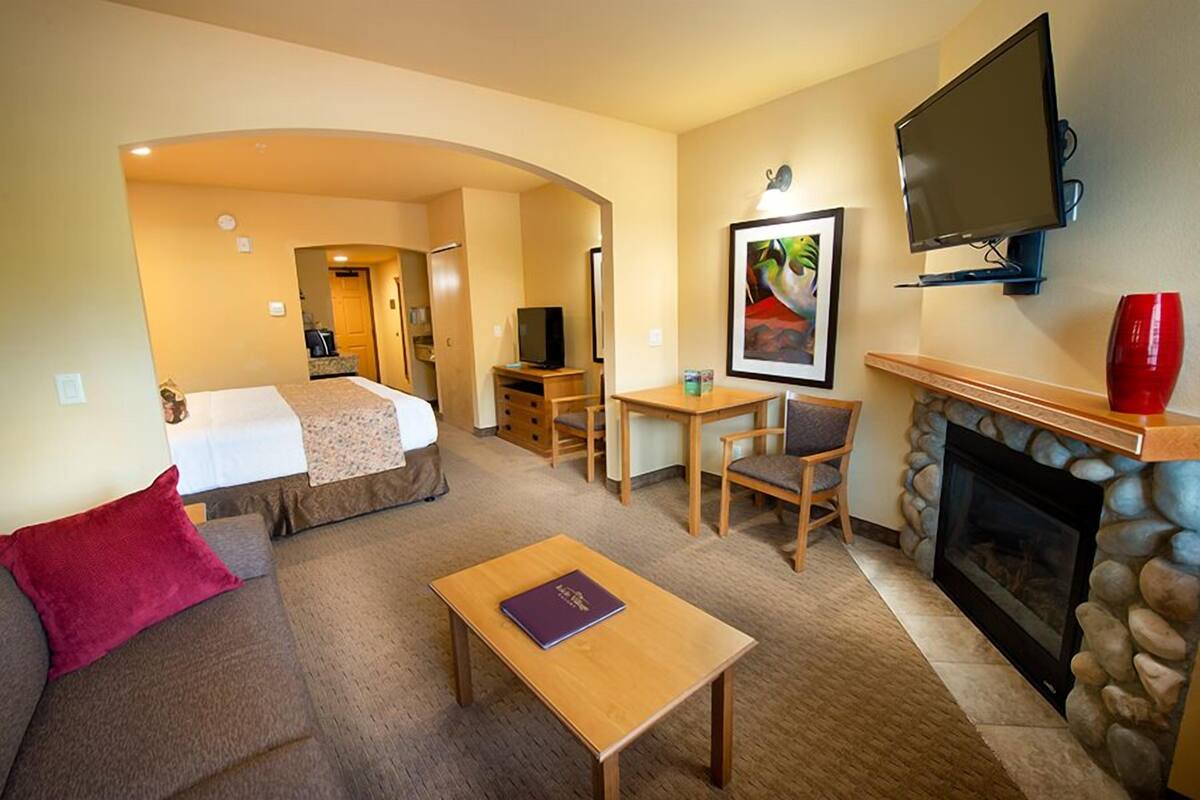 A hotel room with a bed, a sofa, a TV, a fireplace, and a dining area.