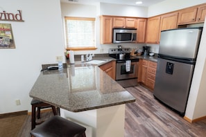 A kitchen with granite countertops, wooden cabinets, a stainless steel refrigerator, and a built-in microwave.