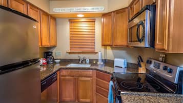 Una cocina con armarios de madera, un refrigerador de acero inoxidable, un microondas, una estufa y un lavamanos.