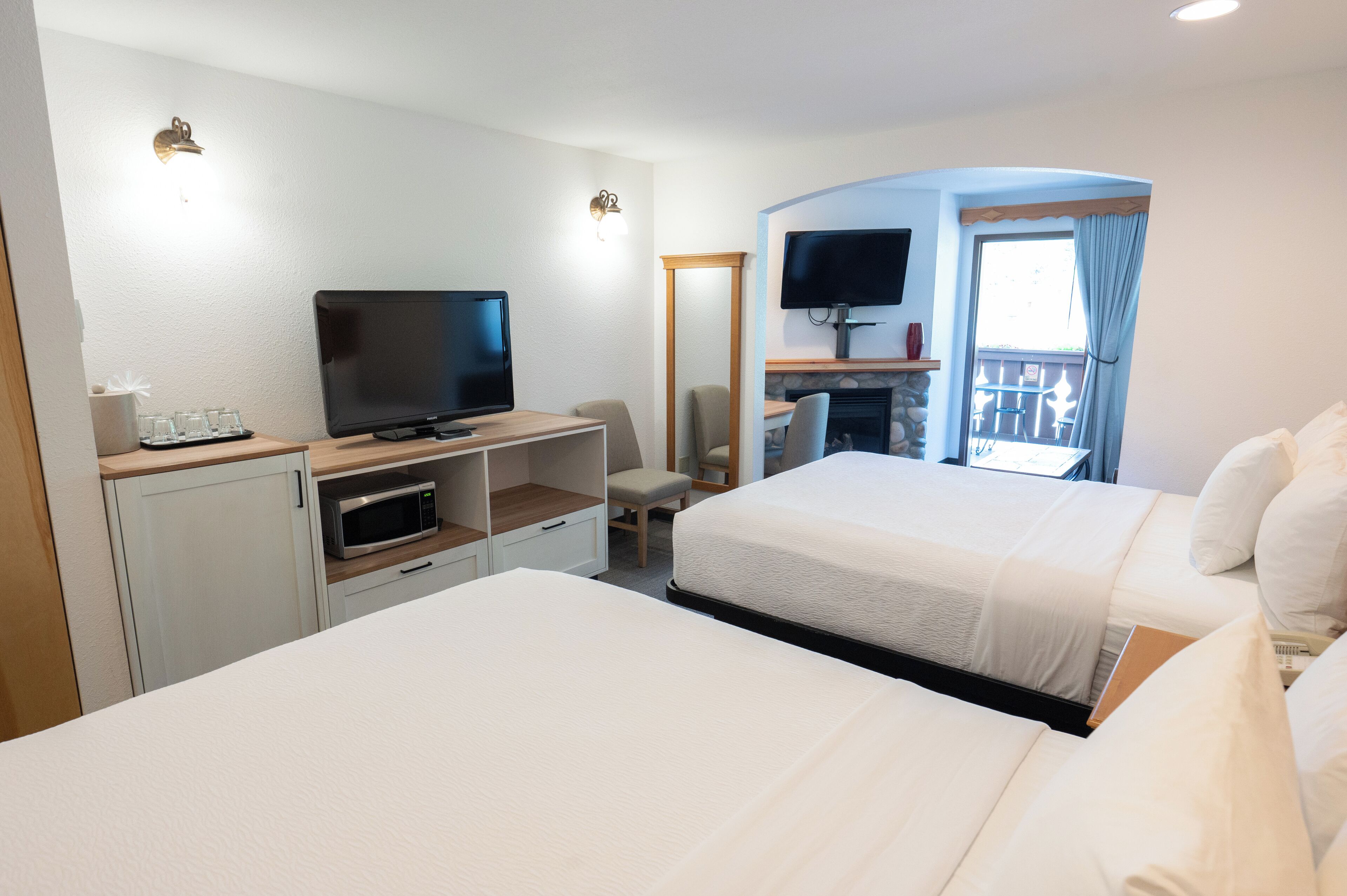 Une chambre d’hôtel avec deux lits, une télévision, un four à micro-ondes, un petit bureau et un balcon équipé d’une télévision.