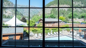 A view through a window of a pool area with lounge chairs, a pool, and a mountainous landscape in the background. - Icicle Village Resort (Leavenworth)