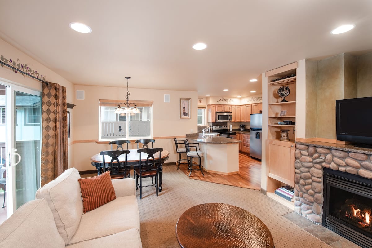 A spacious living room with a fireplace, a dining area, and a kitchen.