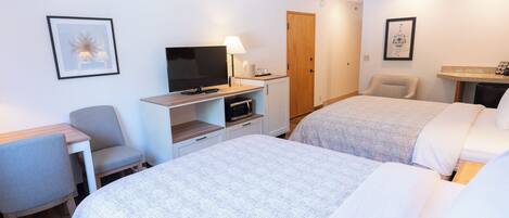 A hotel room with two beds, a desk with a TV, a chair, and a small table with a lamp.