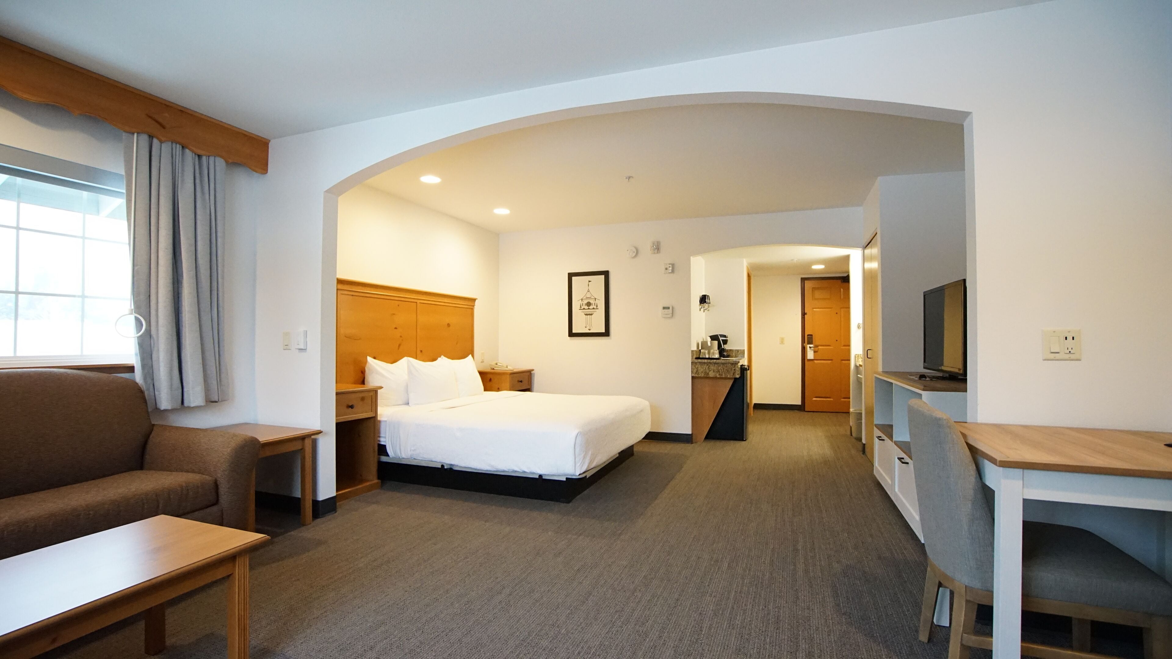 A hotel room with a bed, a desk, a chair, a sofa, and a kitchenette.