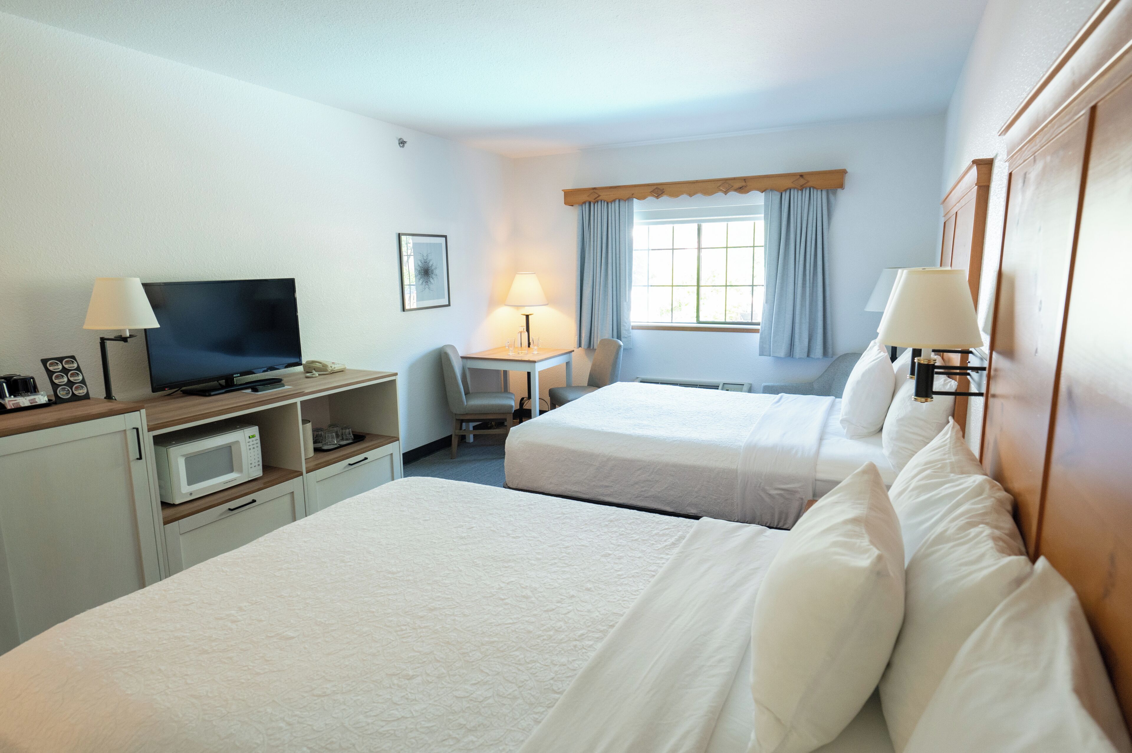 A hotel room with two beds, a desk with a TV, a microwave, and a chair.