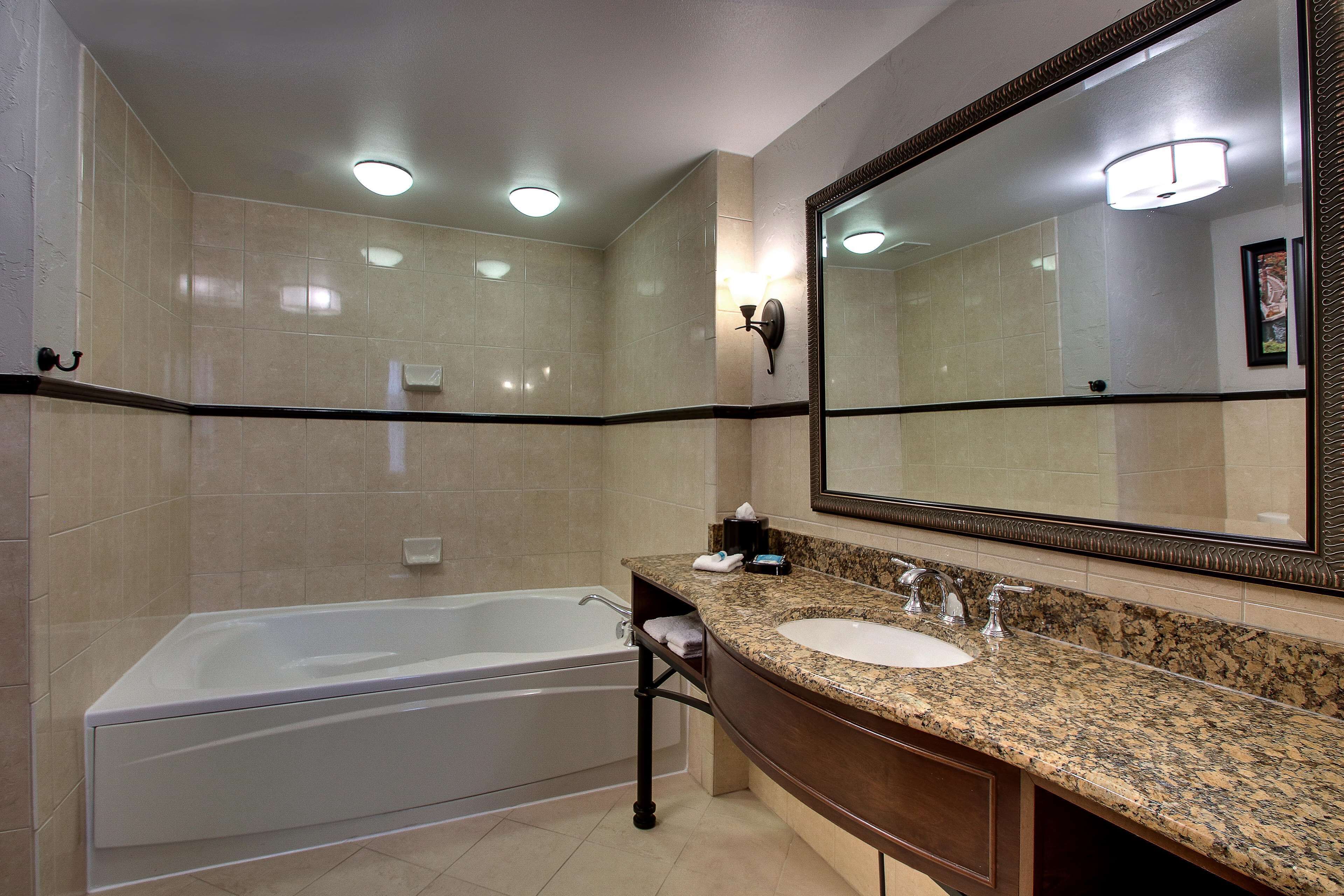 Une salle de bain moderne avec une grande baignoire, un lavabo surmonté d’un plan de travail en granit et un grand miroir.