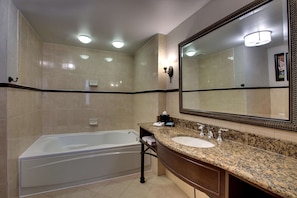 A modern bathroom with a large bathtub, a granite countertop sink, and a large mirror.
