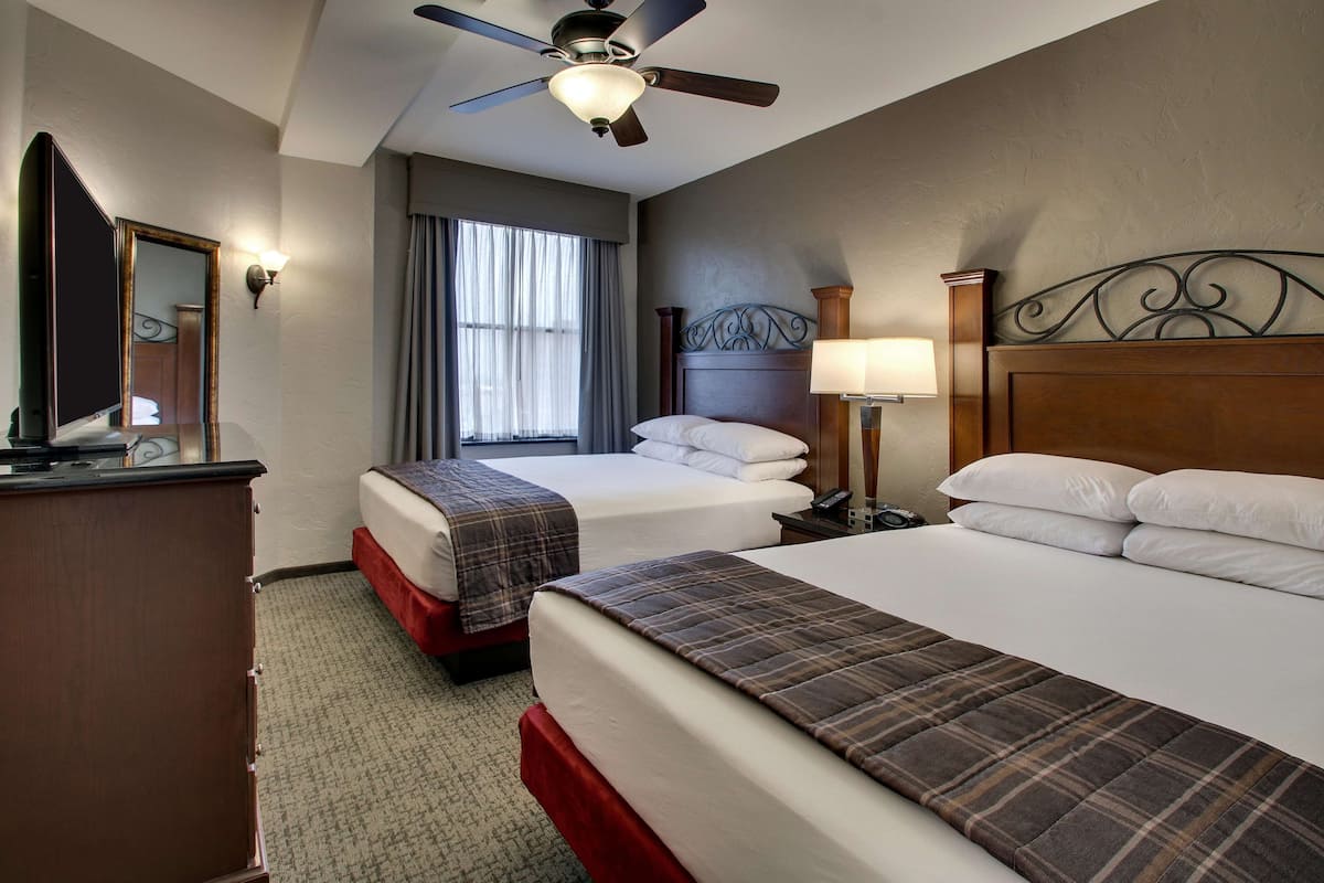 Une chambre d’hôtel avec deux lits, un ventilateur de plafond, un grand miroir et une fenêtre avec des rideaux.
