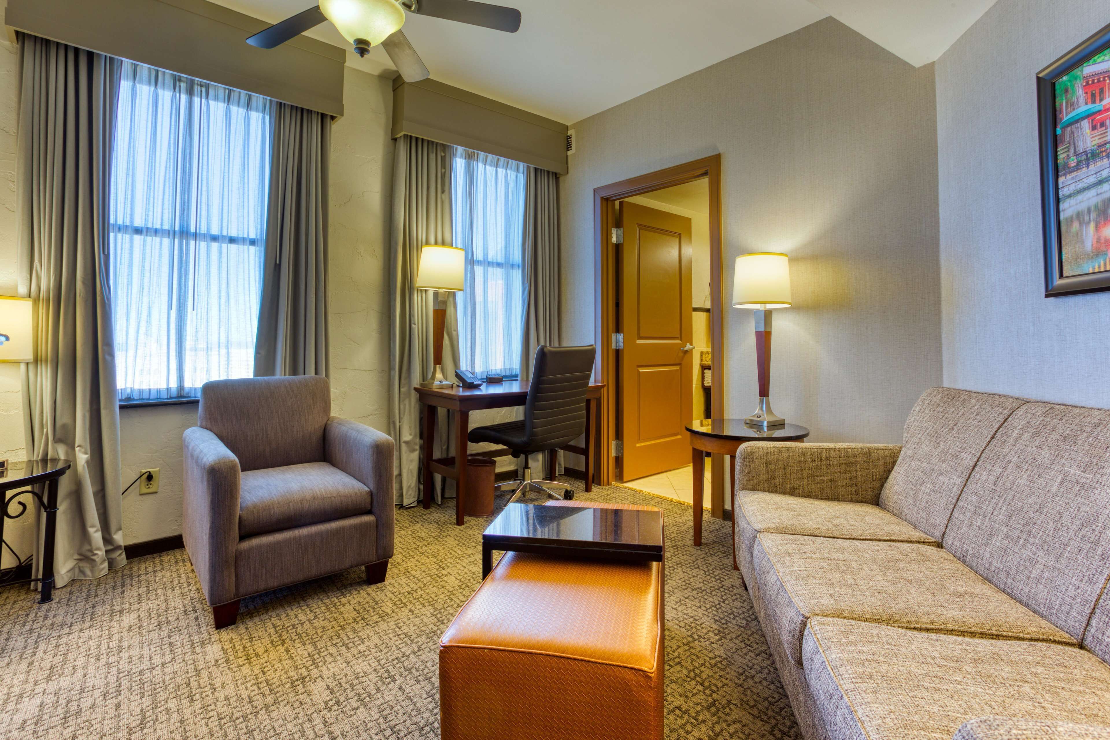 A hotel room with a sofa, armchair, desk, and two lamps.