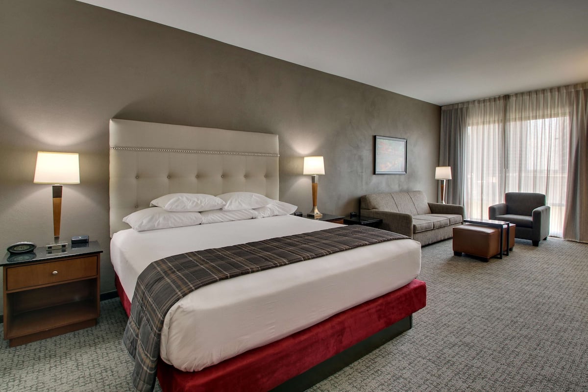 Une chambre d’hôtel avec un grand lit, deux tables de chevet, un canapé, un fauteuil et un sol recouvert de moquette.