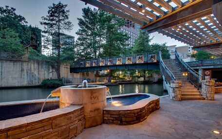 An outdoor pool area with a stone wall, a water fountain, and a bridge connecting different levels.