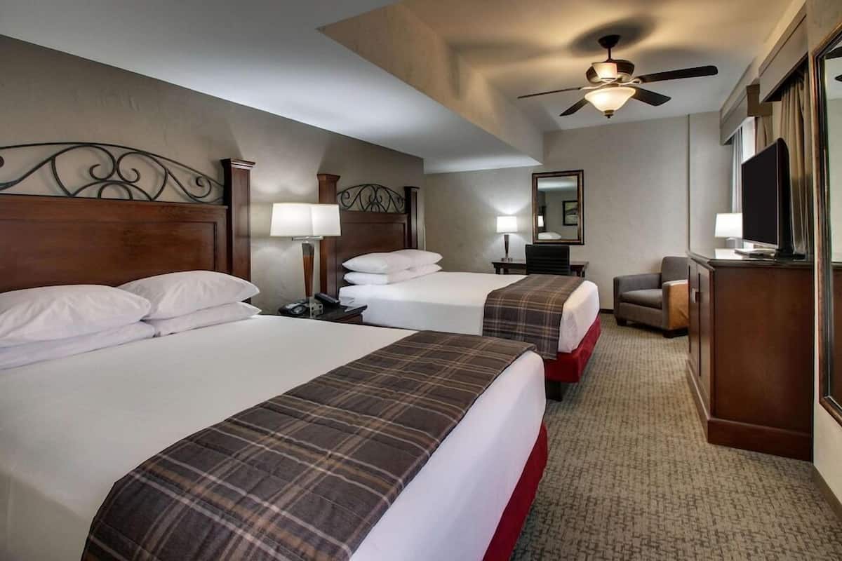 A hotel room with two beds, a ceiling fan, a TV, and a desk with a chair.