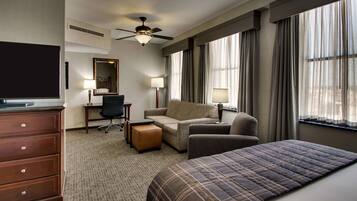 A hotel room with a bed, a desk, a chair, a sofa, a dresser, and a TV.