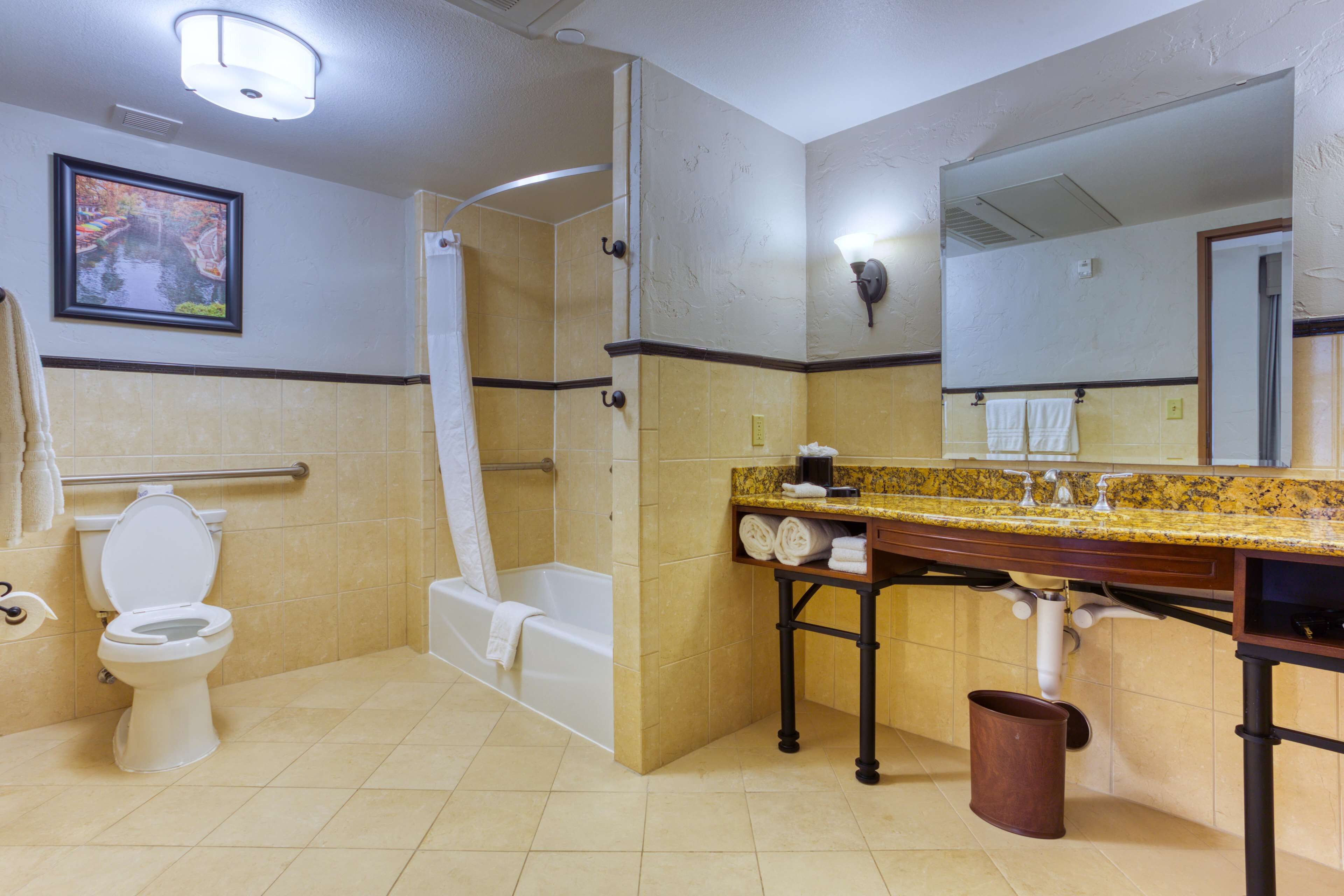 A bathroom with a toilet, bathtub, shower, vanity with a mirror, and a towel rack.
