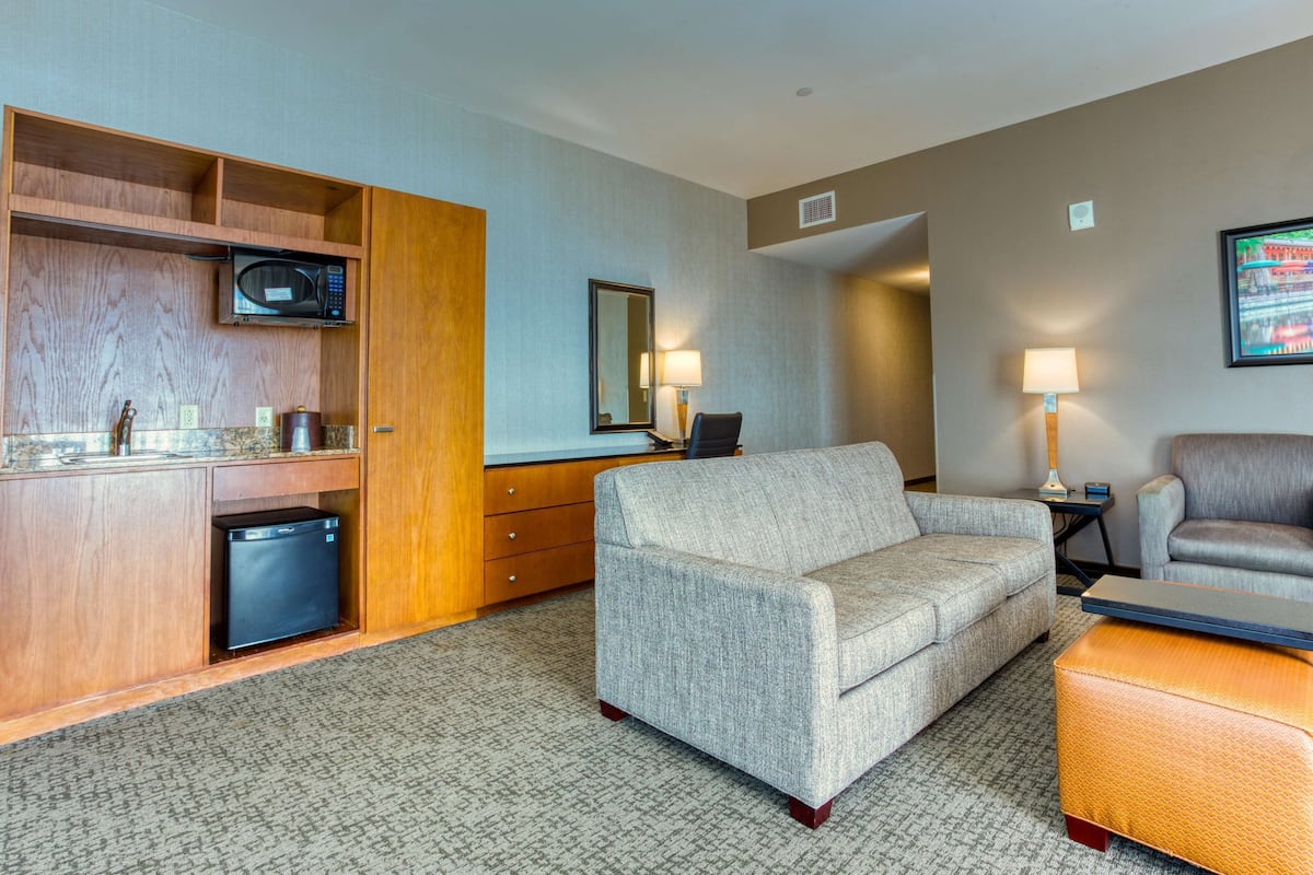 Une chambre d’hôtel équipée d’une kitchenette, d’un canapé, d’un fauteuil et d’une petite table.