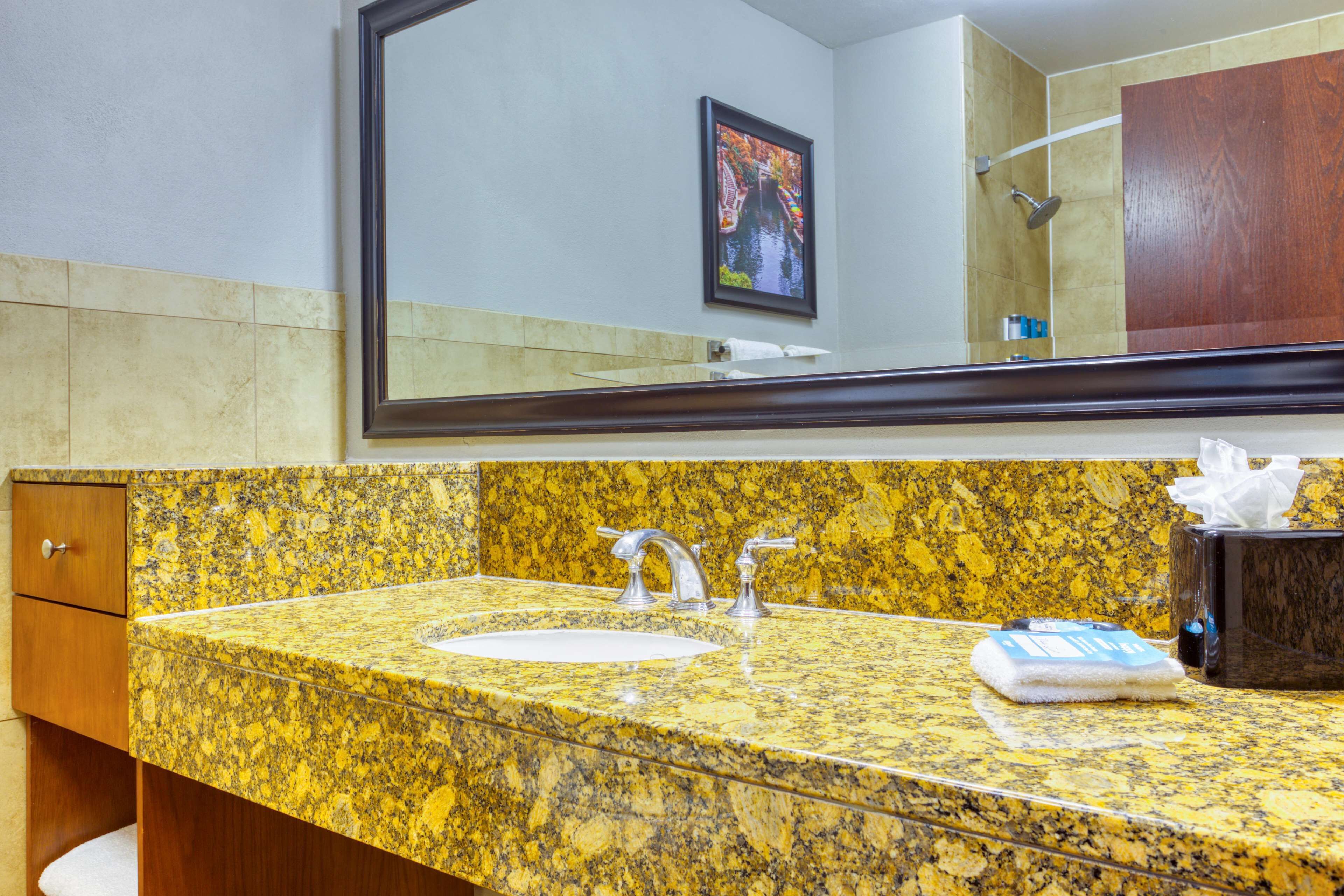 A bathroom with a granite countertop, a sink, a mirror, and a wooden cabinet.