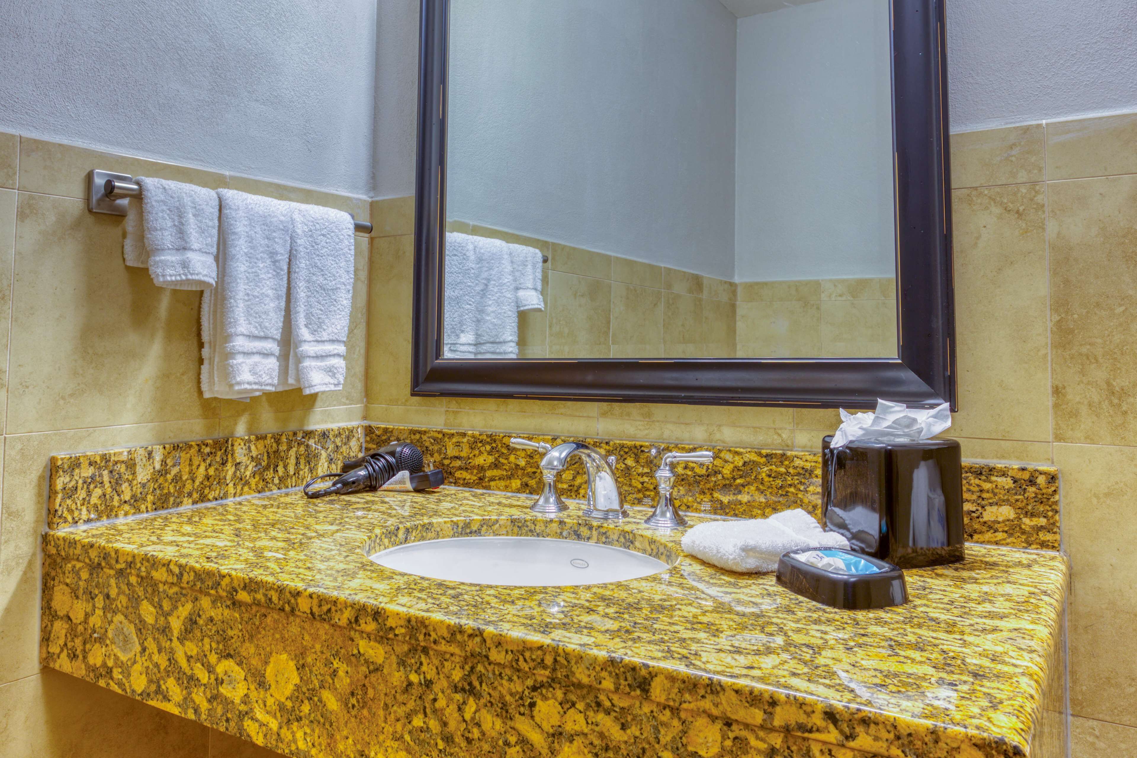 A bathroom with a granite countertop sink, two faucets, a mirror, and a towel rack with two towels.