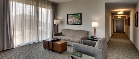 A hotel room with a large window, a sofa, a chair, a small table, and a lamp.