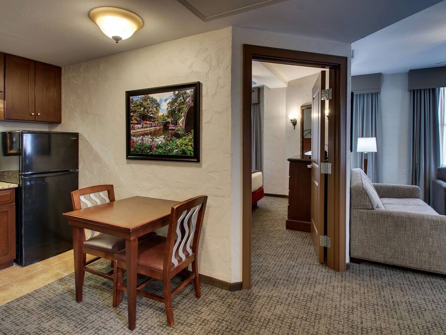 A hotel room with a dining area, a kitchenette, a living area with a sofa, and a door leading to another room.