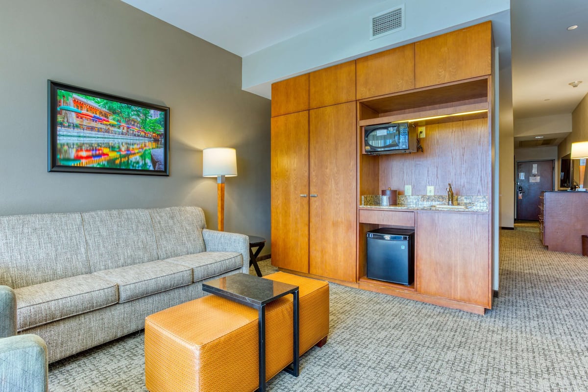 Une chambre d’hôtel comprenant un canapé, une petite table, un meuble avec un téléviseur et un coin cuisine.
