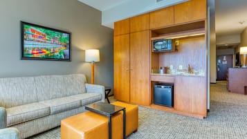 A hotel room with a sofa, a small table, a cabinet with a television, and a kitchenette area.