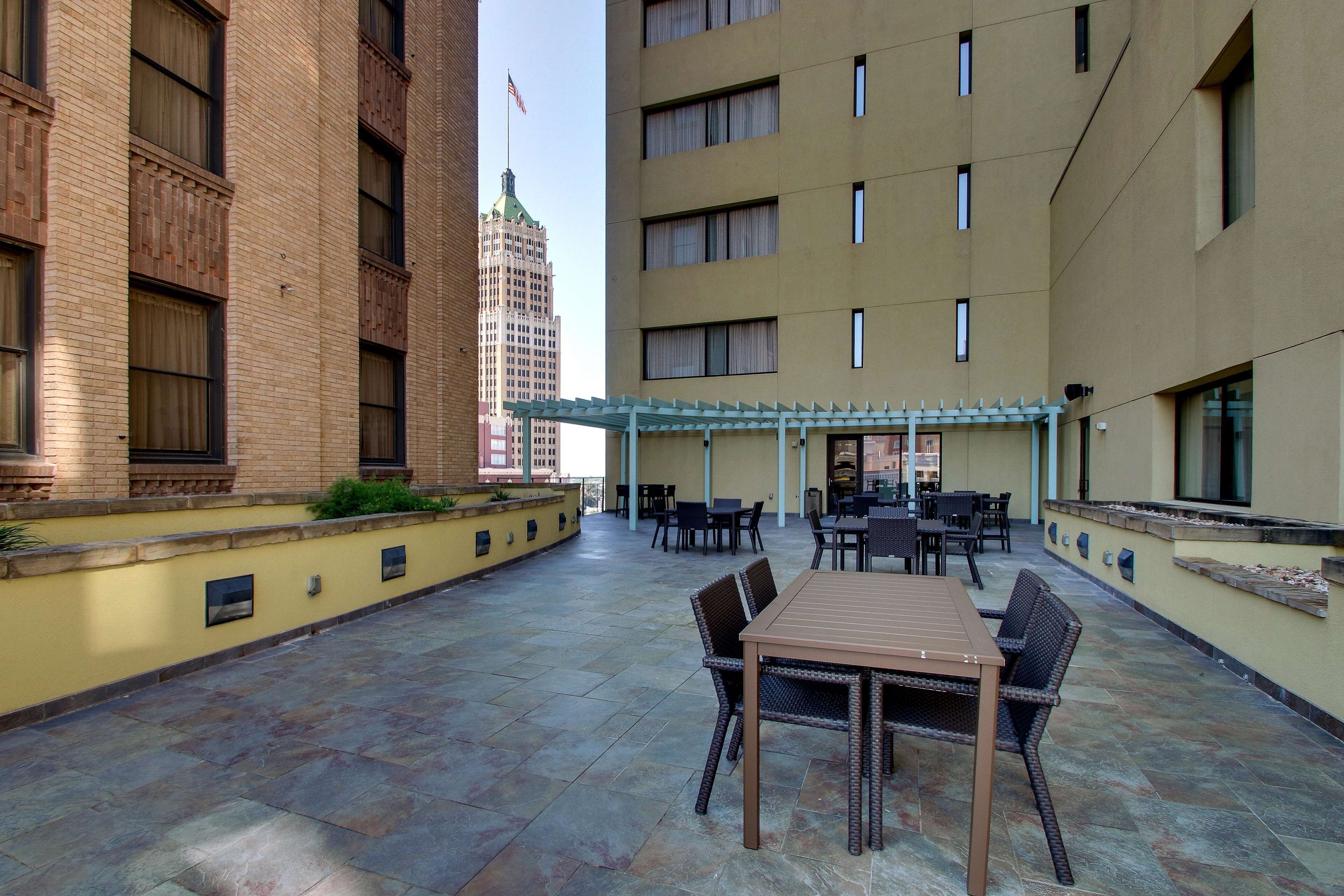 Un'area patio esterna con tavolo e sedie, un pergolato e vista su un alto edificio con bandiera americana.