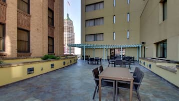 Un'area patio esterna con tavolo e sedie, un pergolato e vista su un alto edificio con bandiera americana.