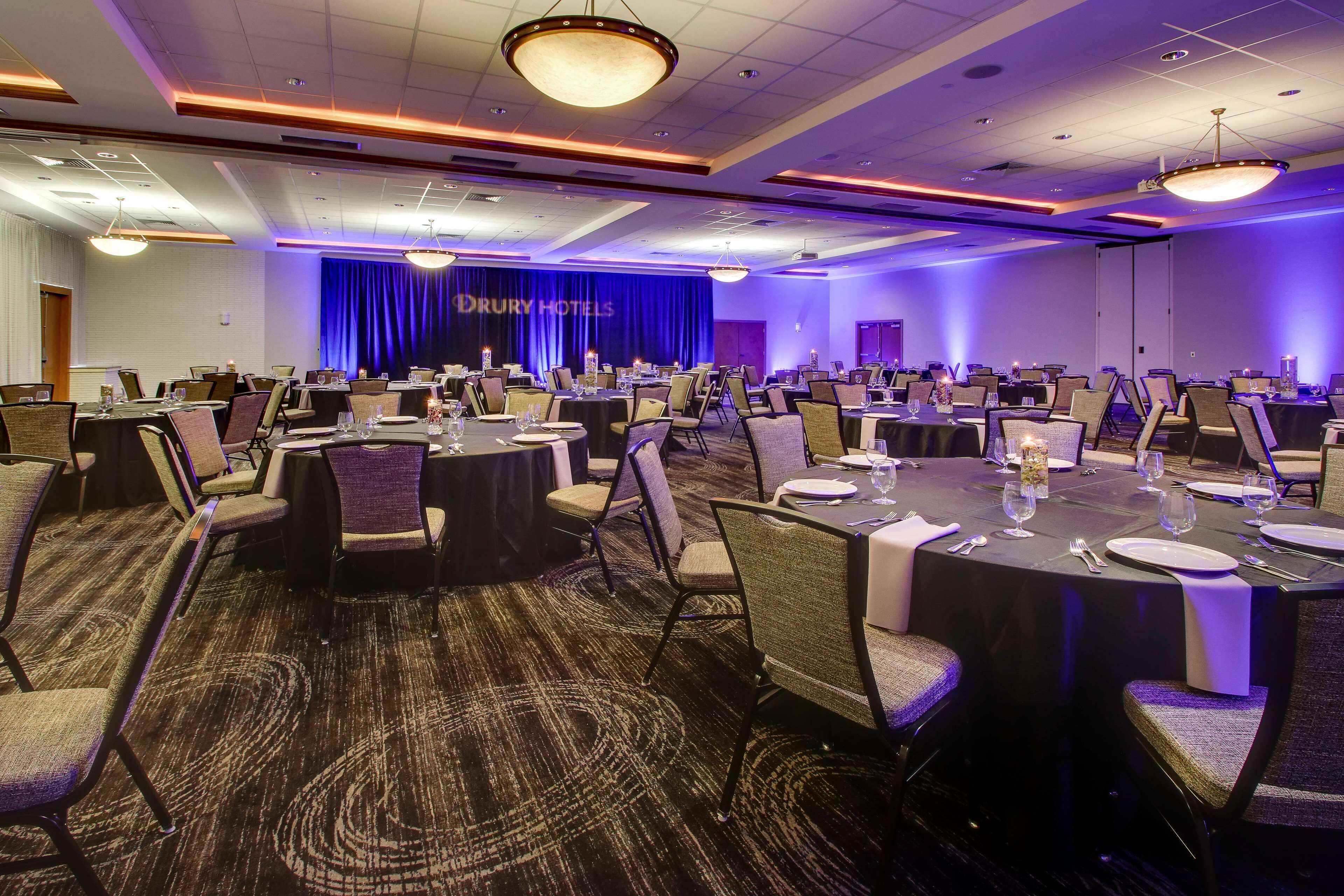 A conference room with round tables, chairs, and a stage with a blue curtain.