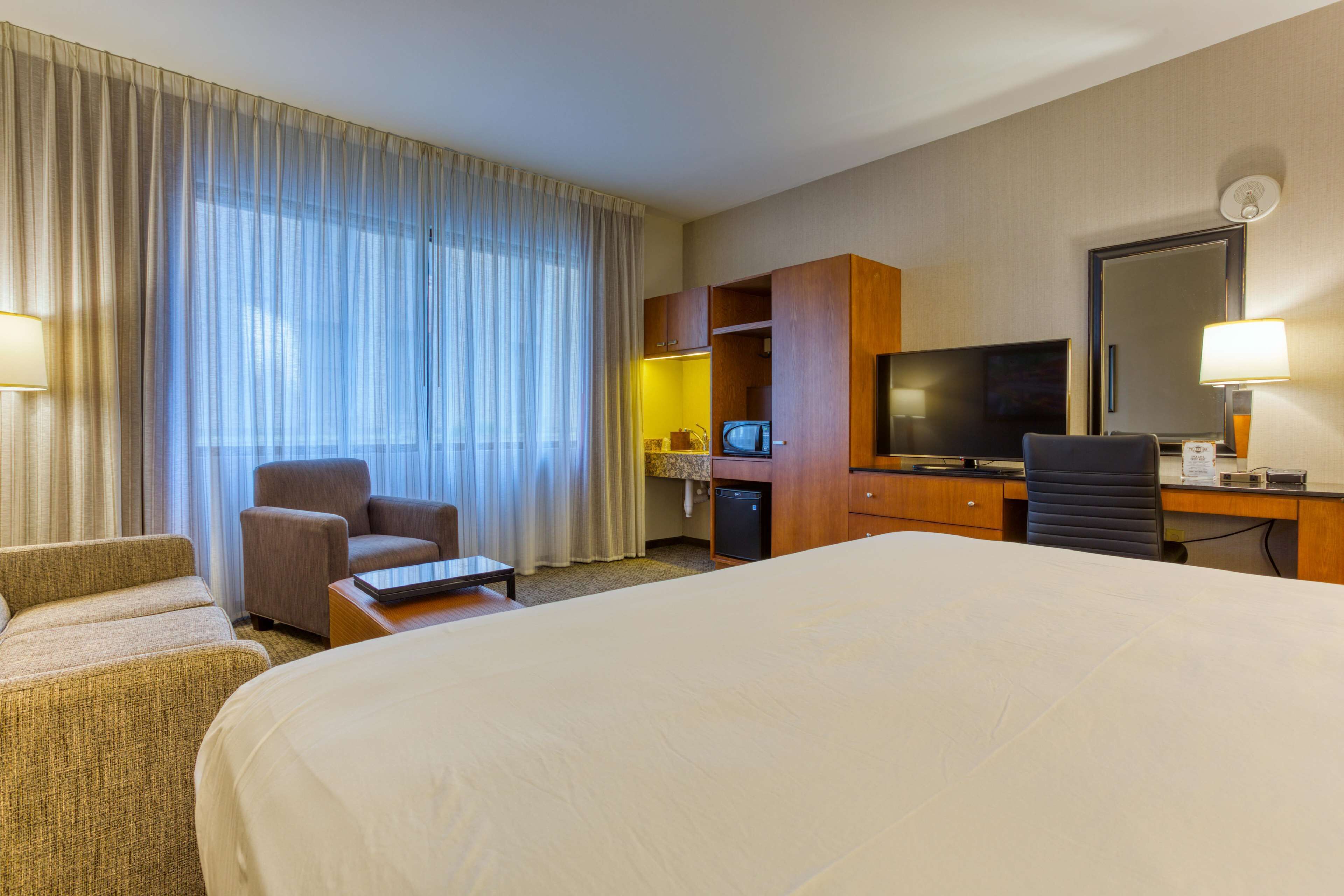 Habitación de hotel con una cama grande, un escritorio con computadora y televisor, una silla y una mesita.