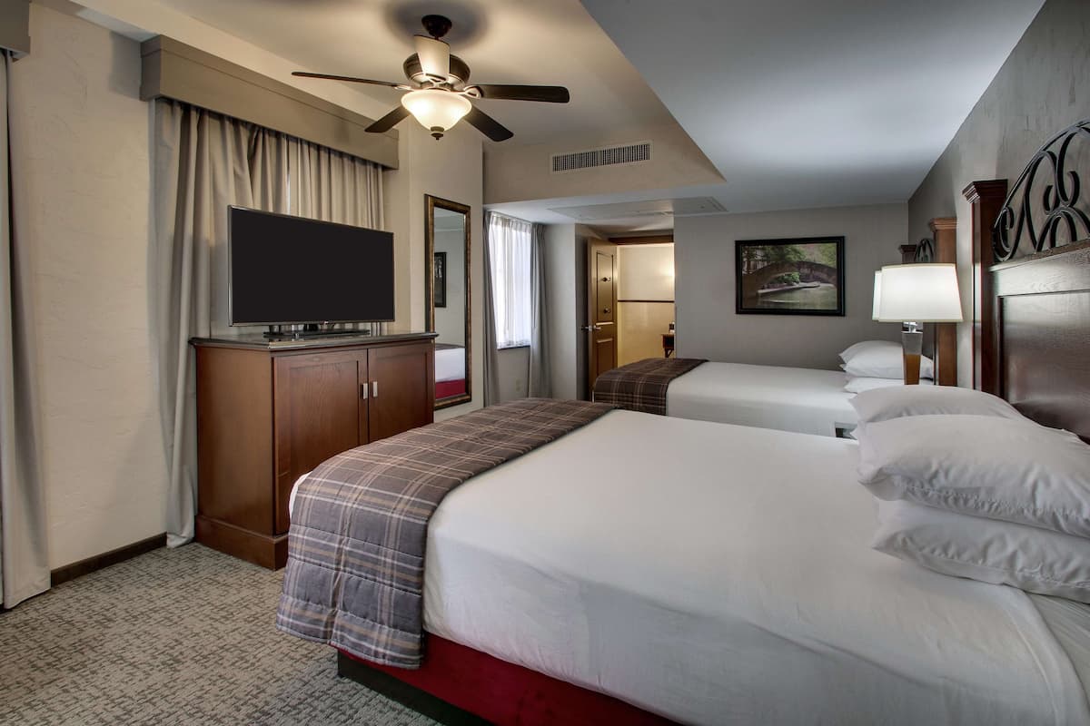 Une chambre d’hôtel avec un grand lit, une télévision, un ventilateur de plafond et un tableau au mur.