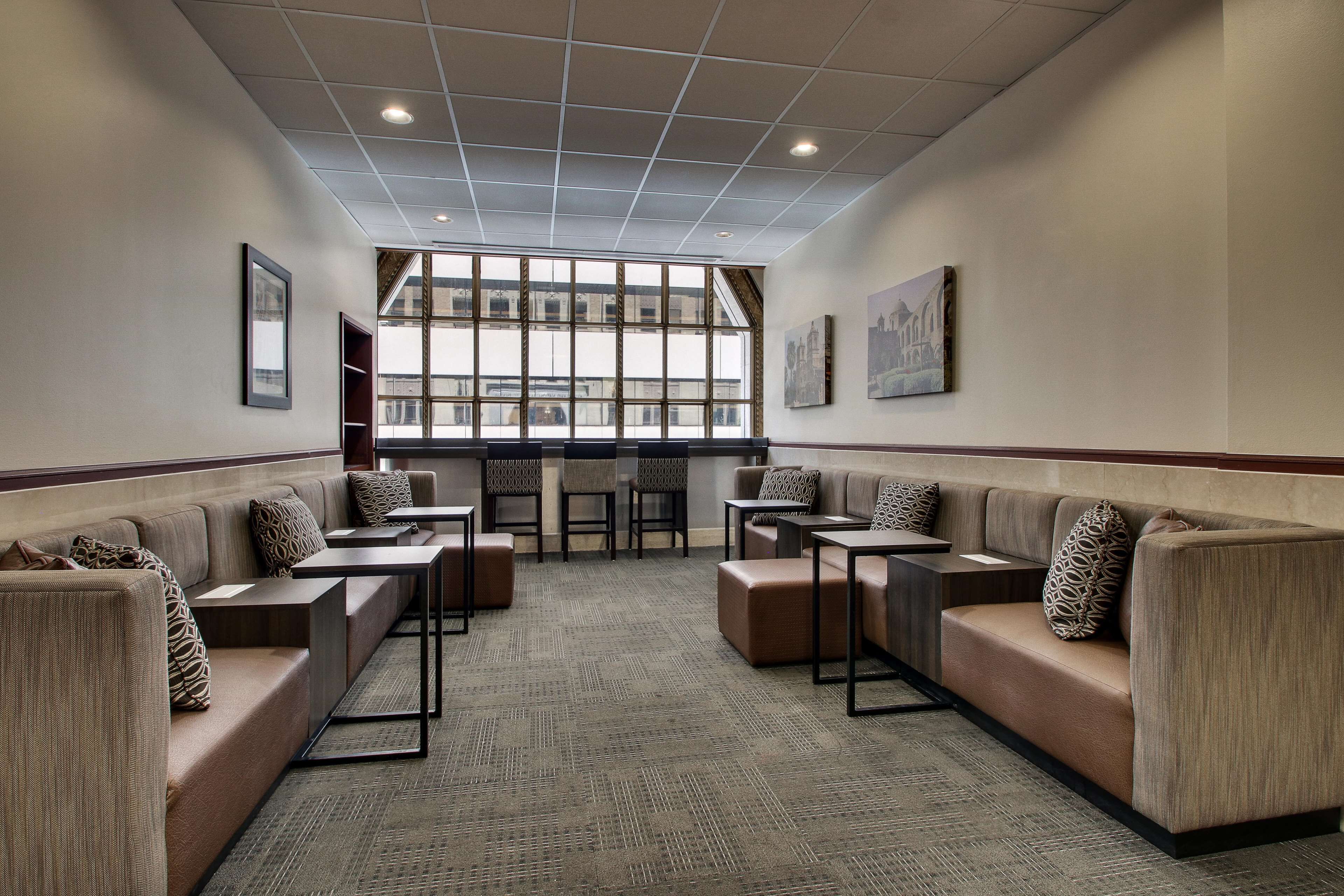 A modern lounge area with cushioned seating, tables, and large windows providing natural light.