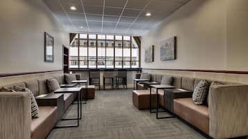 A modern lounge area with cushioned seating, tables, and large windows providing natural light.