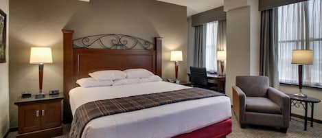 A hotel room with a large bed, two bedside tables, a chair, a ceiling fan, and a window with curtains.