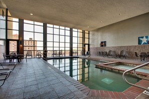 An indoor swimming pool with clear glass walls, tiled floor, and lounge chairs.