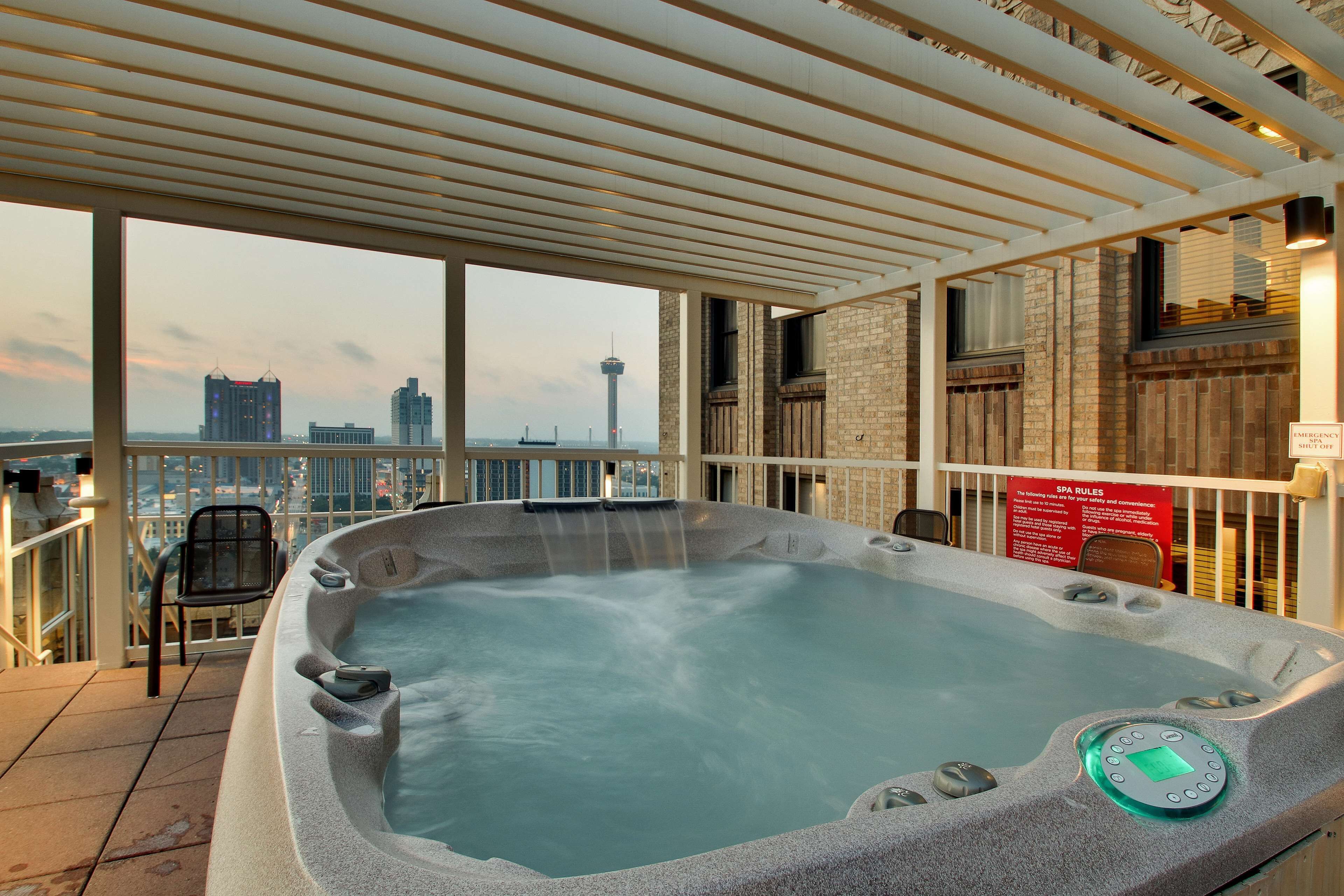 A hot tub with a control panel, a chair, and a view of the cityscape.